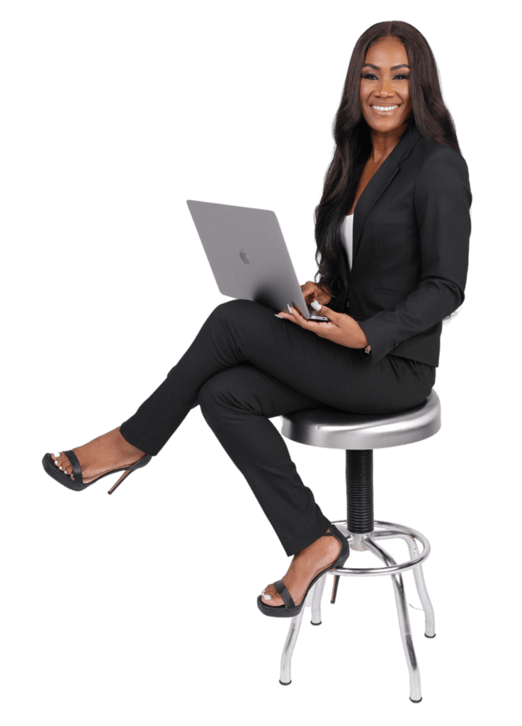 Patrice J White smiling sitting on a silver stool in business attire while holding a laptop